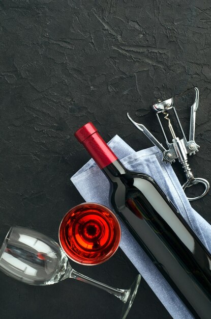 Bottiglia e bicchieri da vino, tappi e cavatappi su sfondo scuro. Vista dall'alto, copia-spazio.