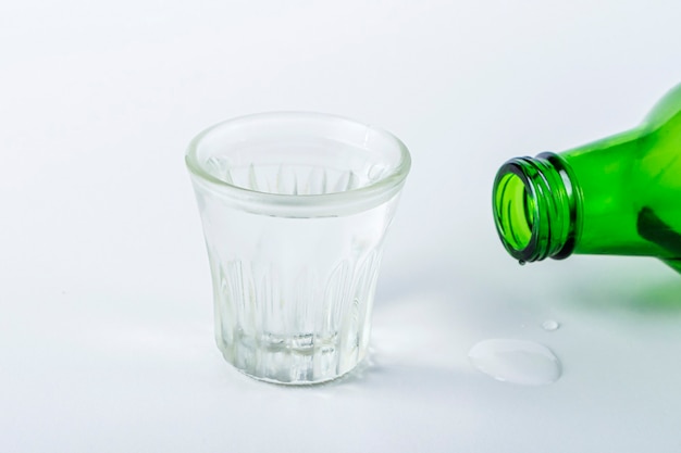 Bottiglia e bicchierino refrigerato di bevanda alcolica sul tavolo bianco. Vodka di riso o vino.