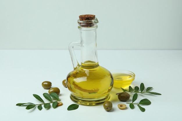 Bottiglia e ciotola di olio, olive e ramoscelli sulla superficie bianca