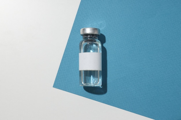 Bottiglia medica in vetro con vaccino su sfondo blu e bianco vista dall'alto