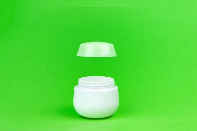 Bottiglia per crema con coperchio volante su sfondo verde. Mockup di imballaggio del barattolo di bottiglia di supplemento.