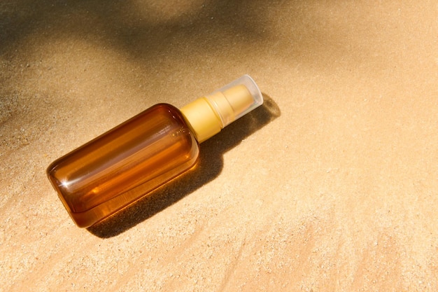 Bottiglia scura senza marchio con olio SPF o crema solare per il corpo su sfondo di spiaggia di sabbia dorata Concetto cosmetico estivo