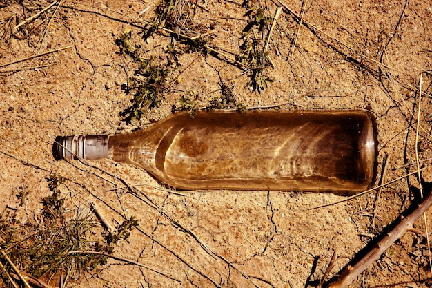 Bottiglia trasparente di vetro sopra il pavimento di argilla in esterno, messaggio di ecologia