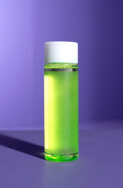 Bottiglia verde di prodotto per la cura cosmetica su sfondo viola con ombra dura