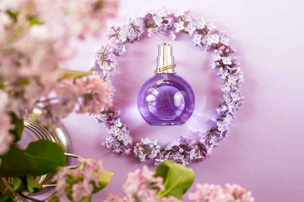 Bottiglia viola di profumo femminile accanto ai fiori di lillà