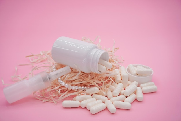 Bottiglie con medicinale, spray nasale. Capsule bianche su sfondo rosa.