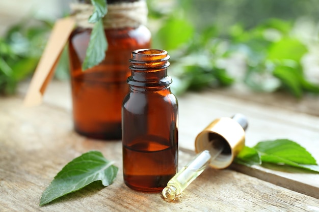 Bottiglie con olio di menta e foglie fresche su fondo di legno