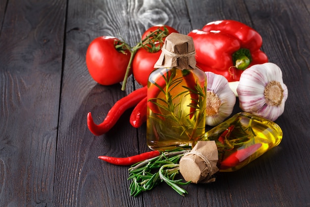 Bottiglie con olio, le erbe e le spezie alla tavola di legno sul nero