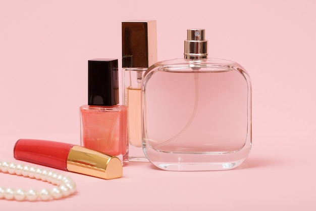 Bottiglie con profumi da donna, smalto per unghie, rossetto e perline su una corda su uno sfondo rosa. Cosmetici e accessori donna.