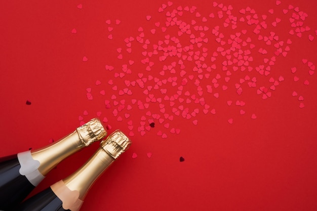 Bottiglie di champagne con cuori di coriandoli su sfondo rosso. Copia spazio, vista dall&#39;alto
