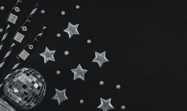 Bottiglie di champagne di carta su cannucce stelle argentate palla da discoteca e palla di neve a sinistra sul nero