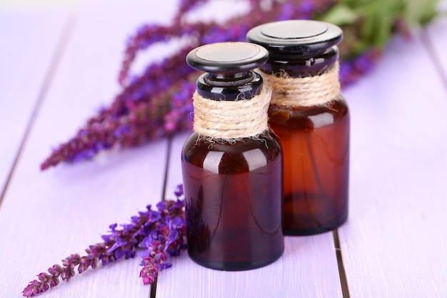 Bottiglie di medicinali e fiori di salvia su fondo di legno viola