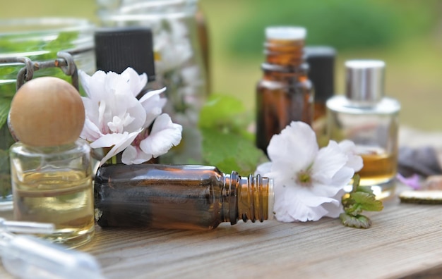 Bottiglie di olio essenziale con piante e fiori su un tavolo di legno in giardino