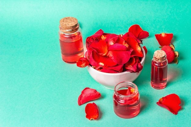 Bottiglie di olio essenziale e petali di rose su sfondo turchese opaco. Spa naturale o concetto di cucina, copia spazio