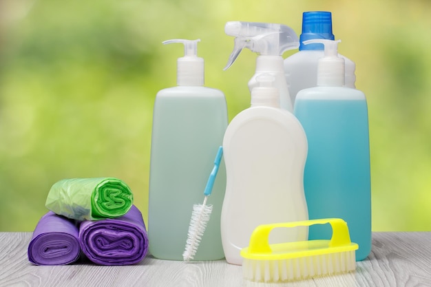 Bottiglie di plastica di detersivo per piatti, detergente per vetri e piastrelle, detergente per forni a microonde e stufe, sacchetti della spazzatura e spazzole sullo sfondo naturale sfocato. Concetto di lavaggio e pulizia.