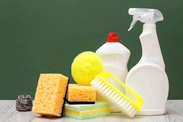 Bottiglie di plastica di detersivo per piatti, detergente per vetri e piastrelle, spazzola gialla e spugne su pavimento in laminato e sfondo verde. Concetto di lavaggio e pulizia.