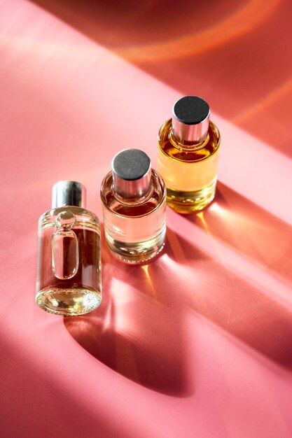 Bottiglie di profumo trasparenti su sfondo rosa Luce e ombre naturali Concetto di essenza femminile e maschile flatlay