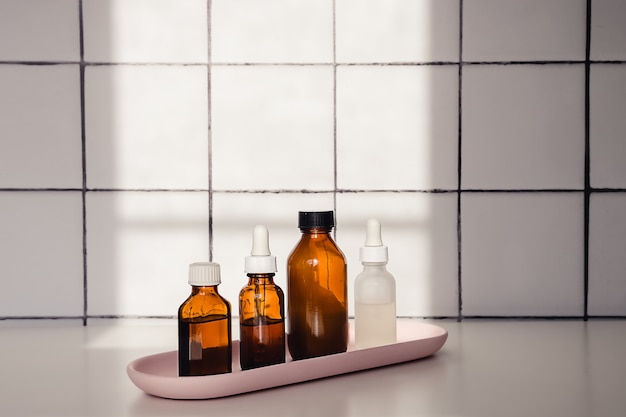 Bottiglie di vetro per cosmetici, medicina naturale, olio essenziale o siero in fila in un vassoio rosa