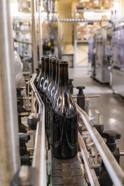 Bottiglie di vetro scuro riempite di vino da imbottigliatrici industriali presso una moderna fabbrica di vino