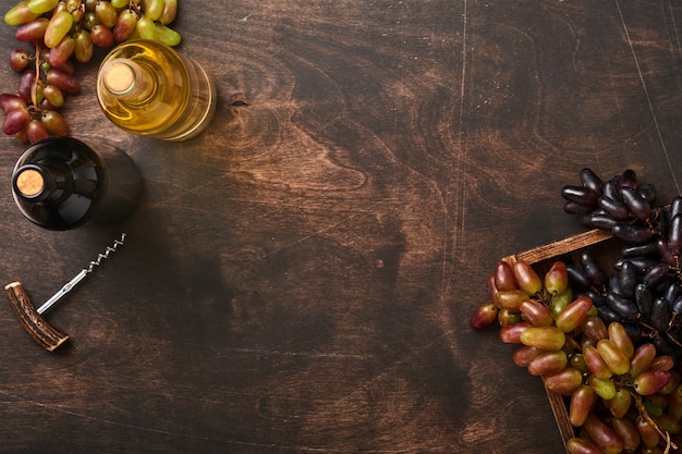 Bottiglie di vino con uva e bicchieri di vino sul vecchio fondo della tavola in legno scuro con spazio per le copie. Vino rosso con un tralcio di vite. Composizione del vino su fondo rustico. Modello.