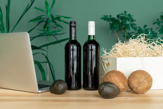 Bottiglie di vino, scatola bianca, computer, noci di cocco e avocado sul tavolo, concetto di ordine online.