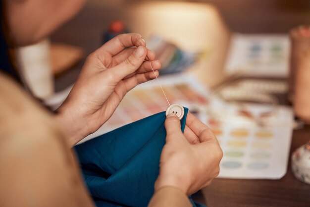 Bottone a mano e cucito con una designer donna che lavora nella moda con un materiale o un prodotto tessile Tavolo creativo e tessuto con un'imprenditrice che lavora in uno studio per cucire o sartoria