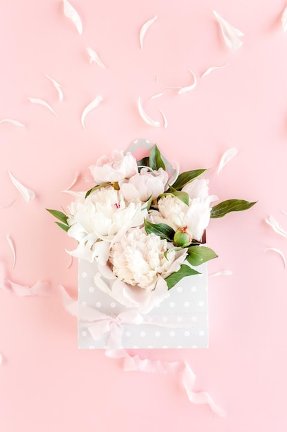 Bouquet beige di peonie in una busta per fiori su sfondo rosa Biglietto d'auguri dal concetto floreale minimo Vista piatta dall'alto
