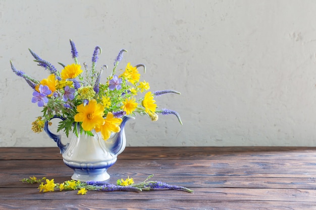 Bouquet con fiori blu e gialli in teiera sul tavolo di legno