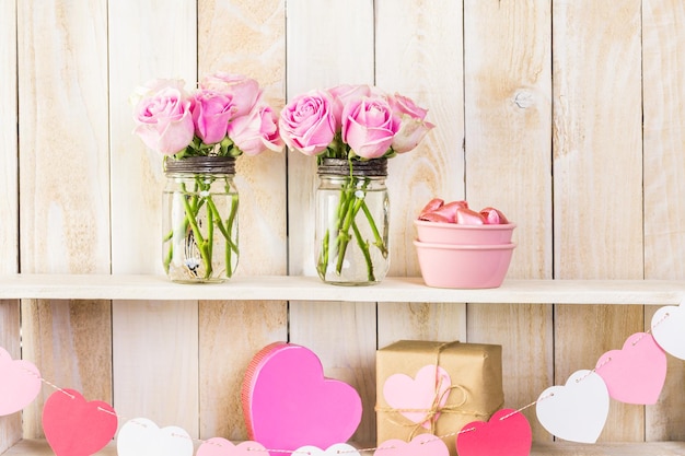 Bouquet con rose rosa in barattolo di vetro su mensola in legno.