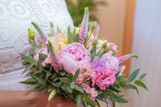 Bouquet da sposa Bellissimo di fiori rosa da sposa nelle mani della sposa Primo piano studio interno girato su sfondo luminoso Bouquet con peonie eustoma ed eremurus