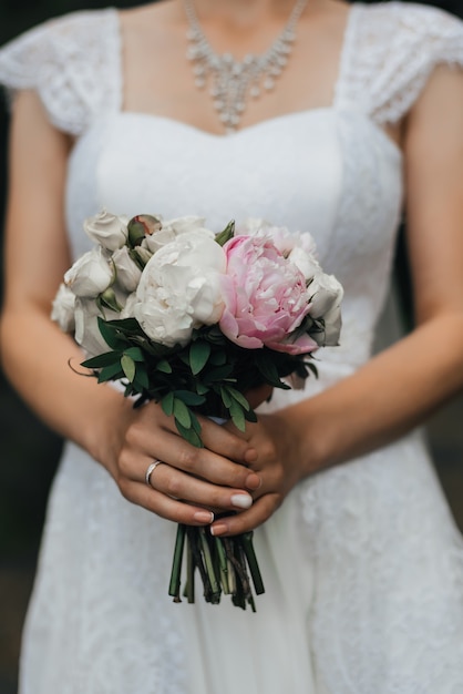 Bouquet da sposa con peonie rosa e rose bianche nelle mani della sposa