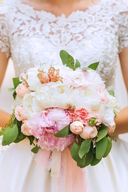 bouquet da sposa delicato e sposa in un abito da sposa con un pizzo rose e peonie