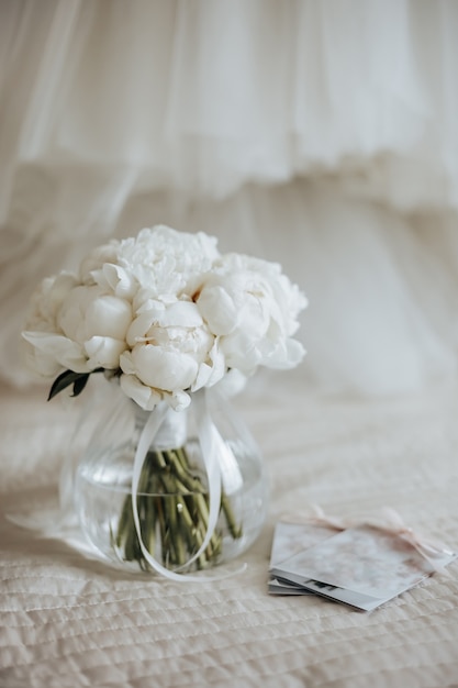 Bouquet da sposa di fiori di peonie in un vaso si trova sul letto degli sposi con inviti