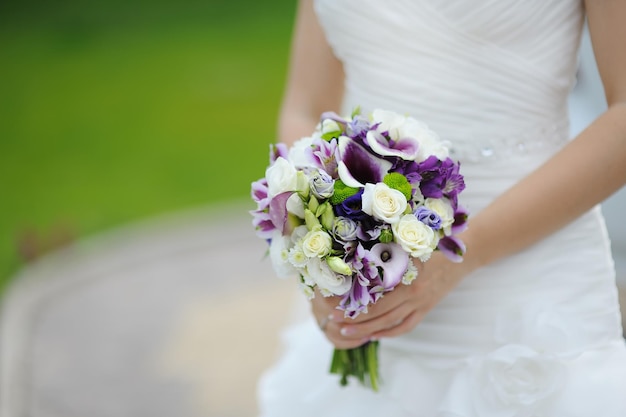 Bouquet da sposa di fiori viola e bianchi nelle mani della sposa