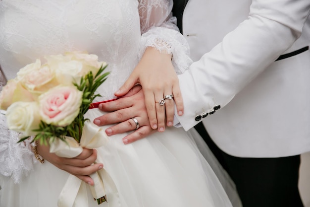 Bouquet da sposa di giorno di nozze nelle mani dei dettagli del primo piano degli anelli di nozze della sposa