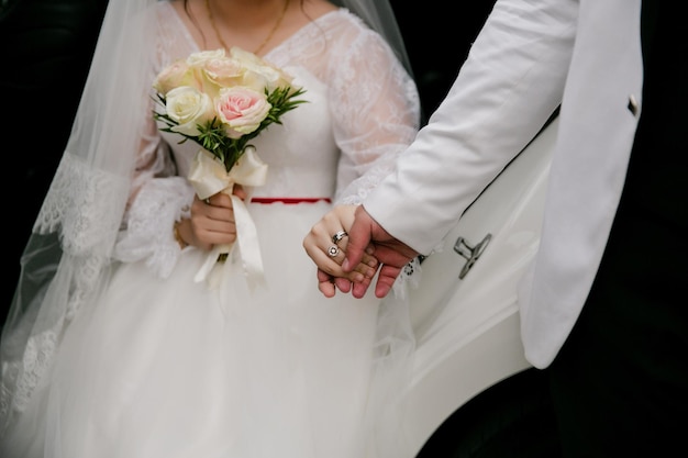 Bouquet da sposa di giorno di nozze nelle mani dei dettagli del primo piano degli anelli di nozze della sposa