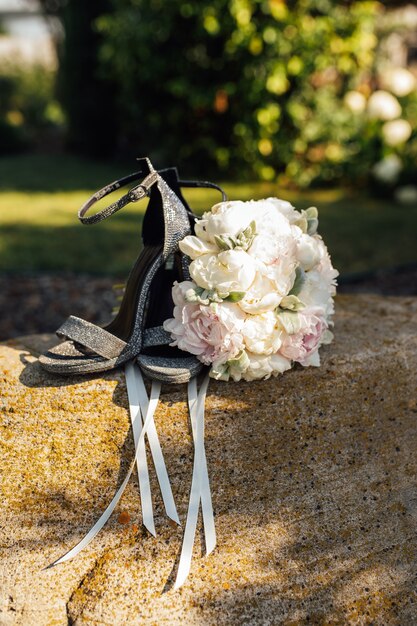 Bouquet da sposa di peonie accanto a scarpe da donna su una pietra.