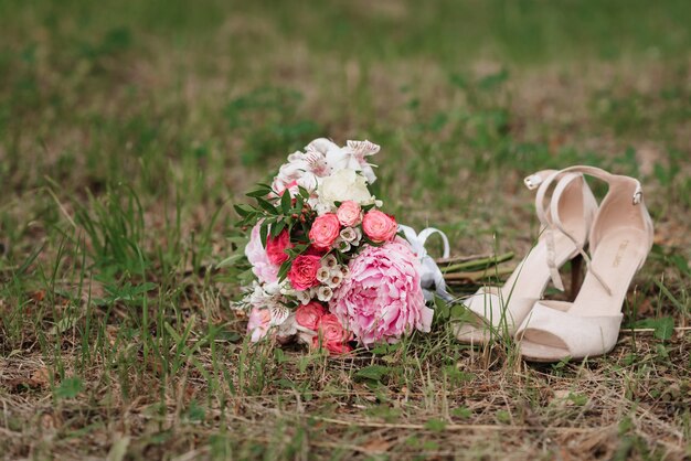 Bouquet da sposa di rose bianche e rosa e peonie con scarpe sdraiato sull'erba