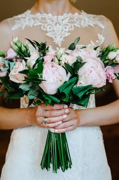 Bouquet da sposa Matrimonio La ragazza in un abito bianco in piedi su uno sfondo marrone e tiene un bel bouquet di fiori rosa bianchi e verde