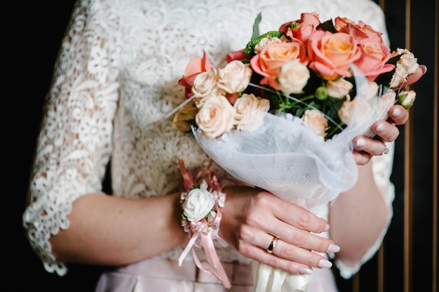 Bouquet da sposa. Nozze. La ragazza in abito bianco in piedi su uno sfondo marrone e tiene in mano un bellissimo mazzo di fiori rosa e verde.