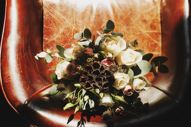 Bouquet da sposa originale composto da rose bianche e fiori secchi si trova sulla sedia in pelle
