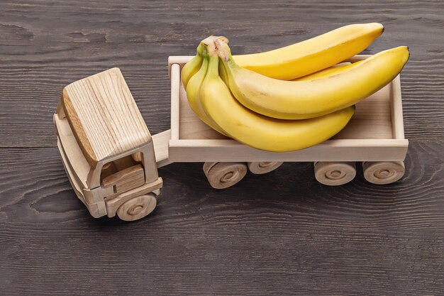 Bouquet di banane mature nel rimorchio del camion, giocattolo in legno. Fondo di legno scuro, colpo dello studio, primo piano.