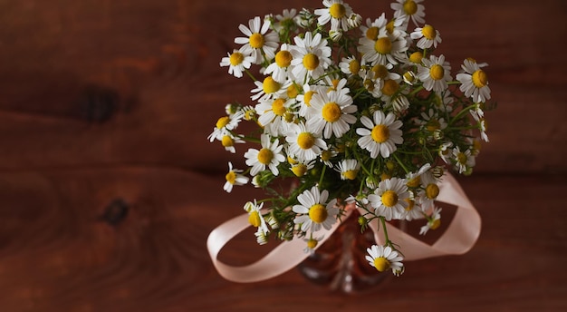 Bouquet di camomiles freschi in fiore con fiocco a nastro su sfondo di legno Bellissimi fiori di camomilla con foglie verdi