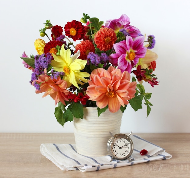 Bouquet di dalie da giardino nel secchio sul tavolo e una sveglia retrò in metallo ancora in vita in stile rustico brillante composizione estiva con fiori e un orologio