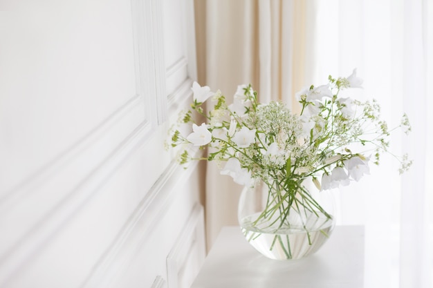 Bouquet di delicate campane in vaso. Luce del mattino nella stanza. Decorazioni per la casa morbide, vaso di vetro con fiori bianchi