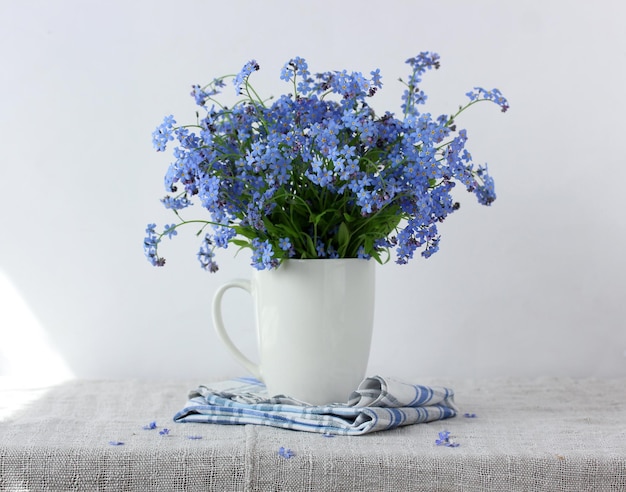 Bouquet di dimenticaremenots blu in una tazza bianca di fiori estivi