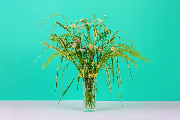 Bouquet di erbe estive, margherite e fiori di clematide in un vaso di vetro di colore menta