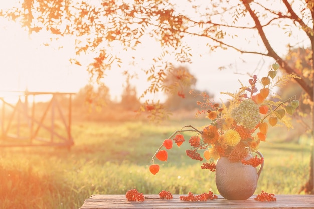 Bouquet di fiori autunnali in brocca rustica sul tavolo di legno all'aperto al tramonto