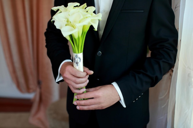 Bouquet di fiori bianchi di calla nelle mani degli sposi e accessori per lo sposo