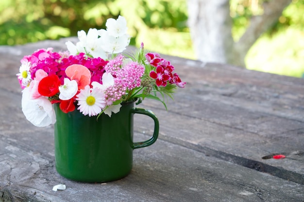 Bouquet di fiori da giardino in tazza smaltata verde sul vecchio tavolo di legno all'aperto